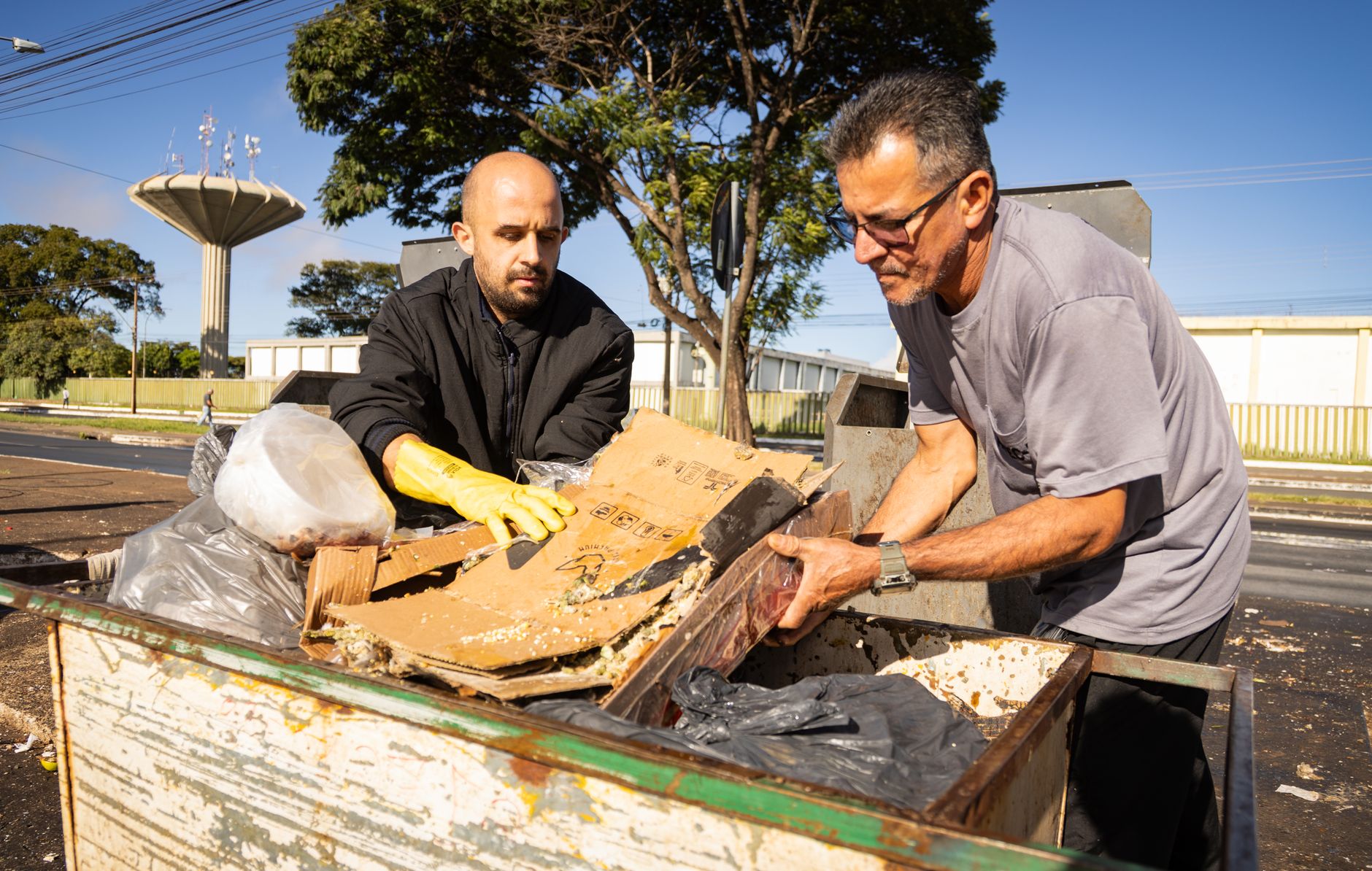 Two men sorting cardboard and plastic at a recycling point in an urban area, emphasizing environmental awareness.