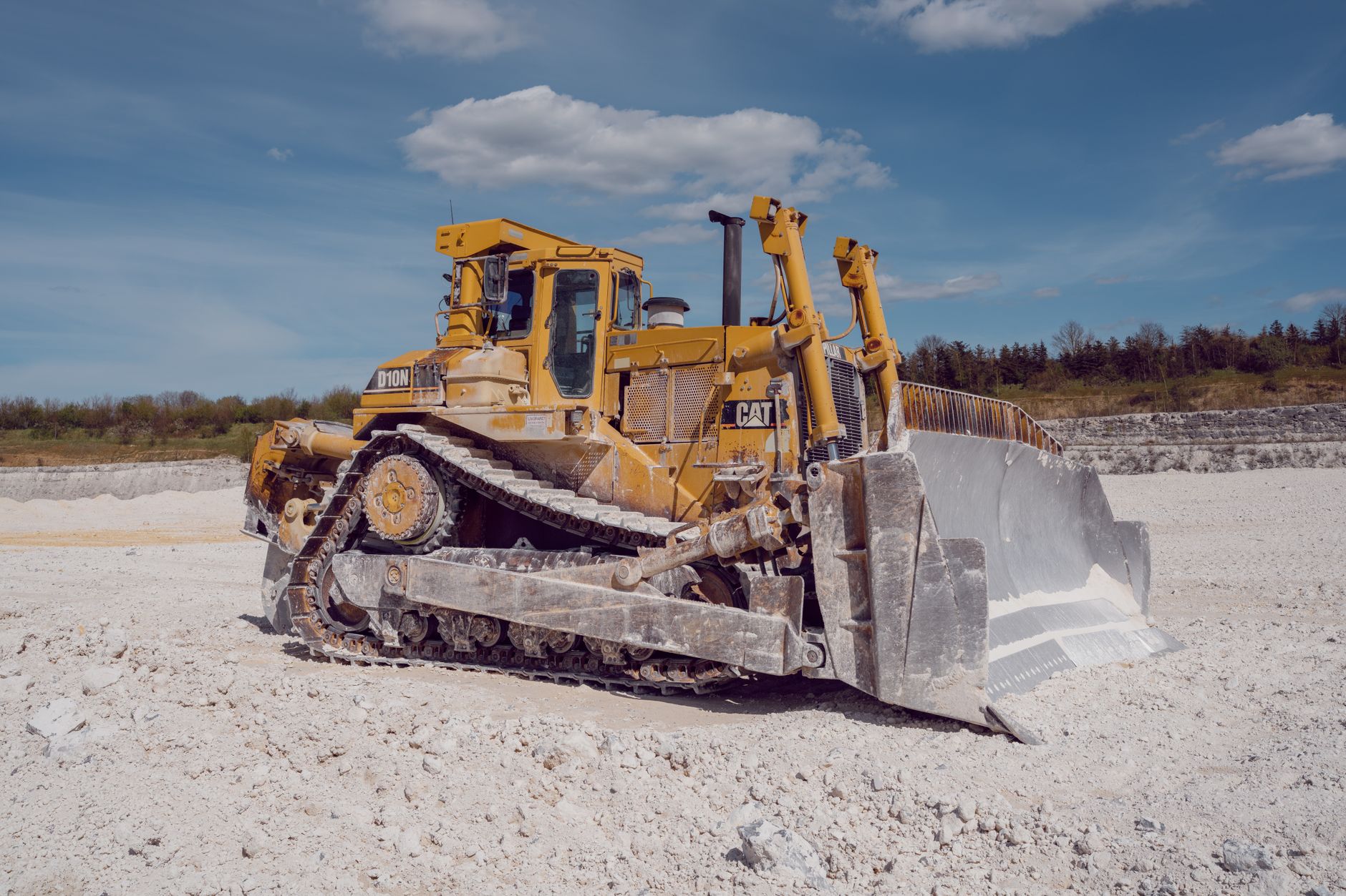 A yellow bulldozer operates in a quarry under a blue sky, showcasing industrial strength.