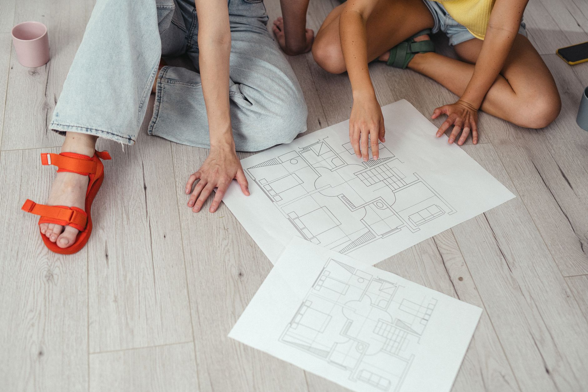 Two people discussing house blueprints on a light wooden floor.