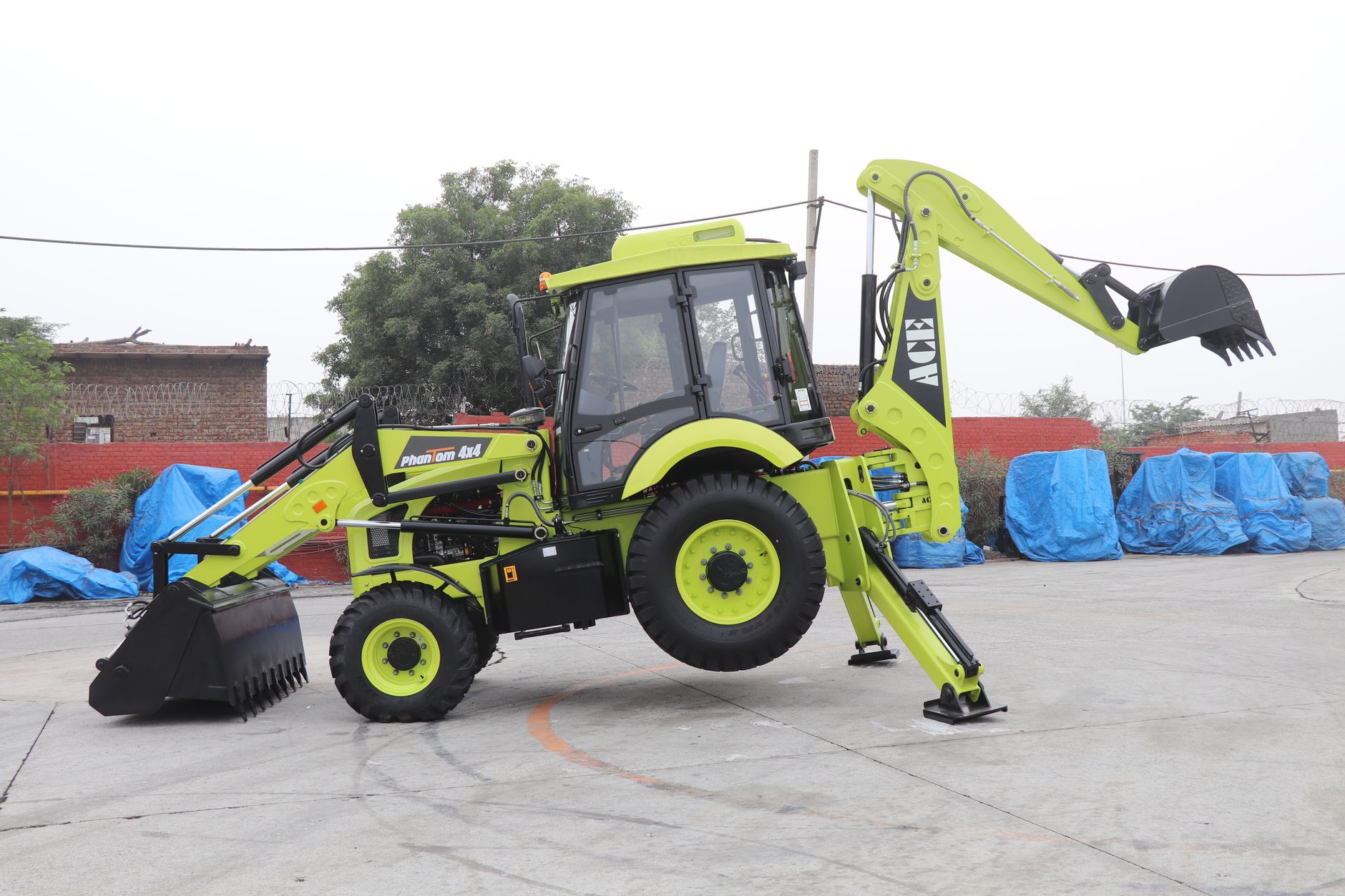 A vibrant ACE Phantom 4x4 backhoe loader is showcased in an outdoor setting in Faridabad, India.