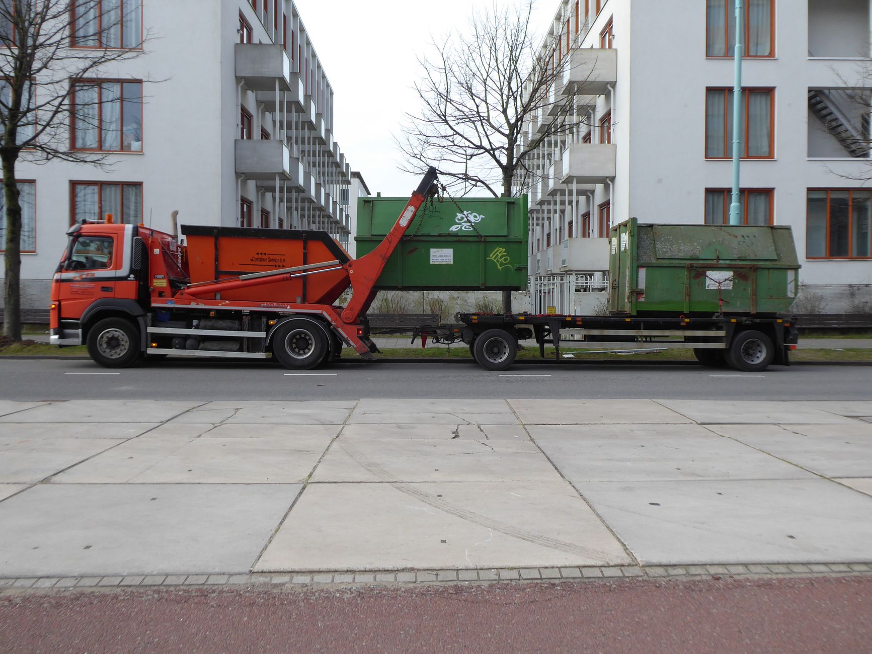 Orange garbage truck with green containers in urban Amsterdam, showcasing industrial city life.
