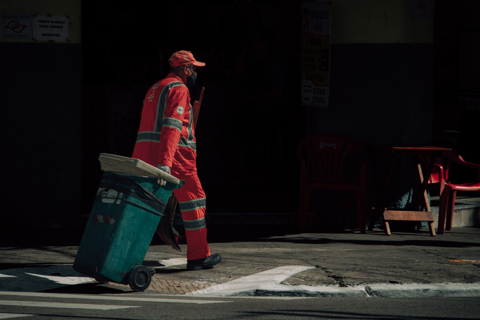 Municipal worker in uniform pulling a trash bin on an urban street.