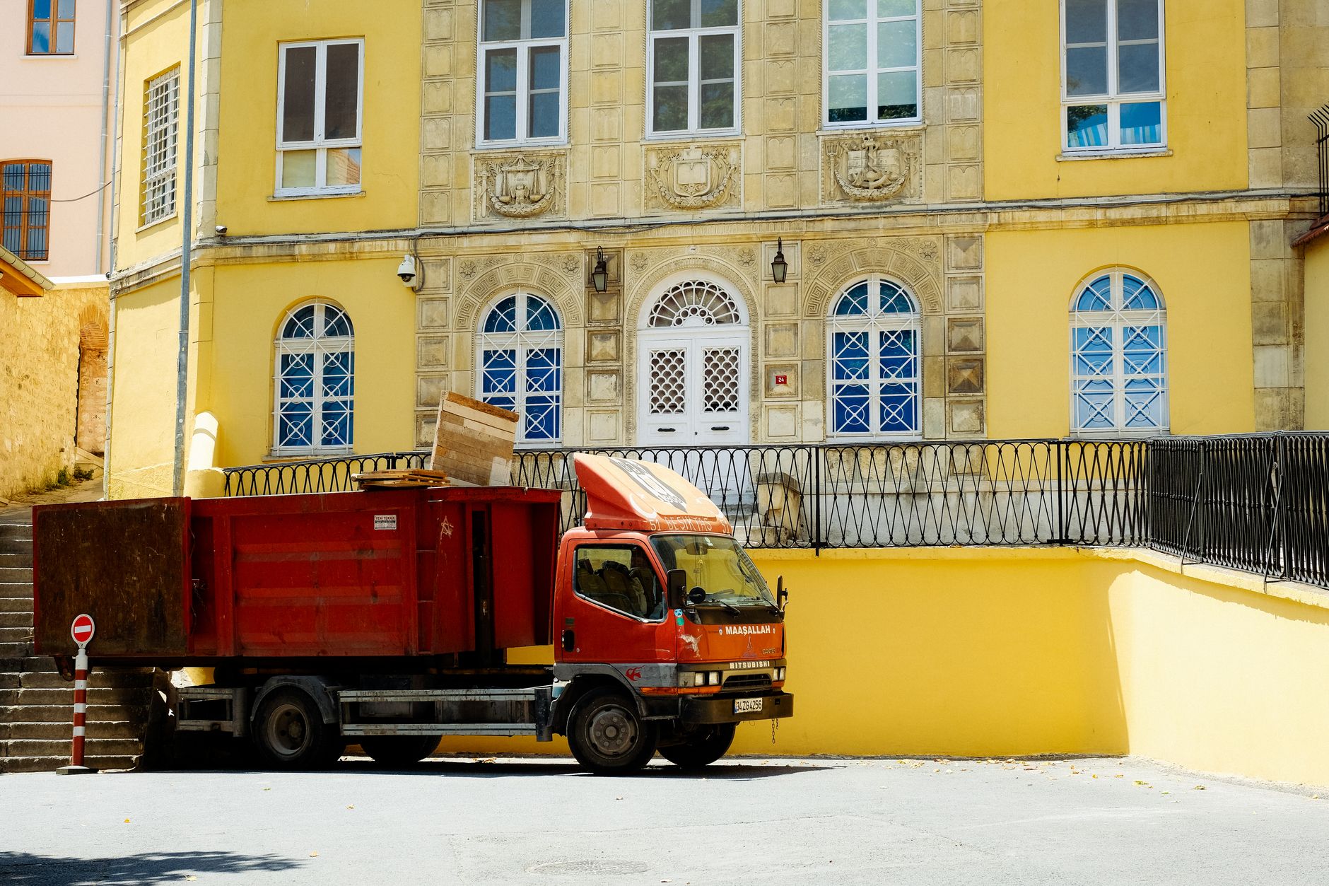 A red truck parked in front of a historic yellow building facade in an urban setting.