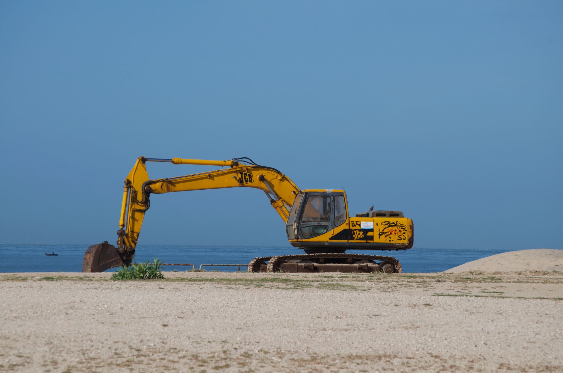 Yellow excavator on a sandy beach in Portugal with a clear blue sky and sea in the background.