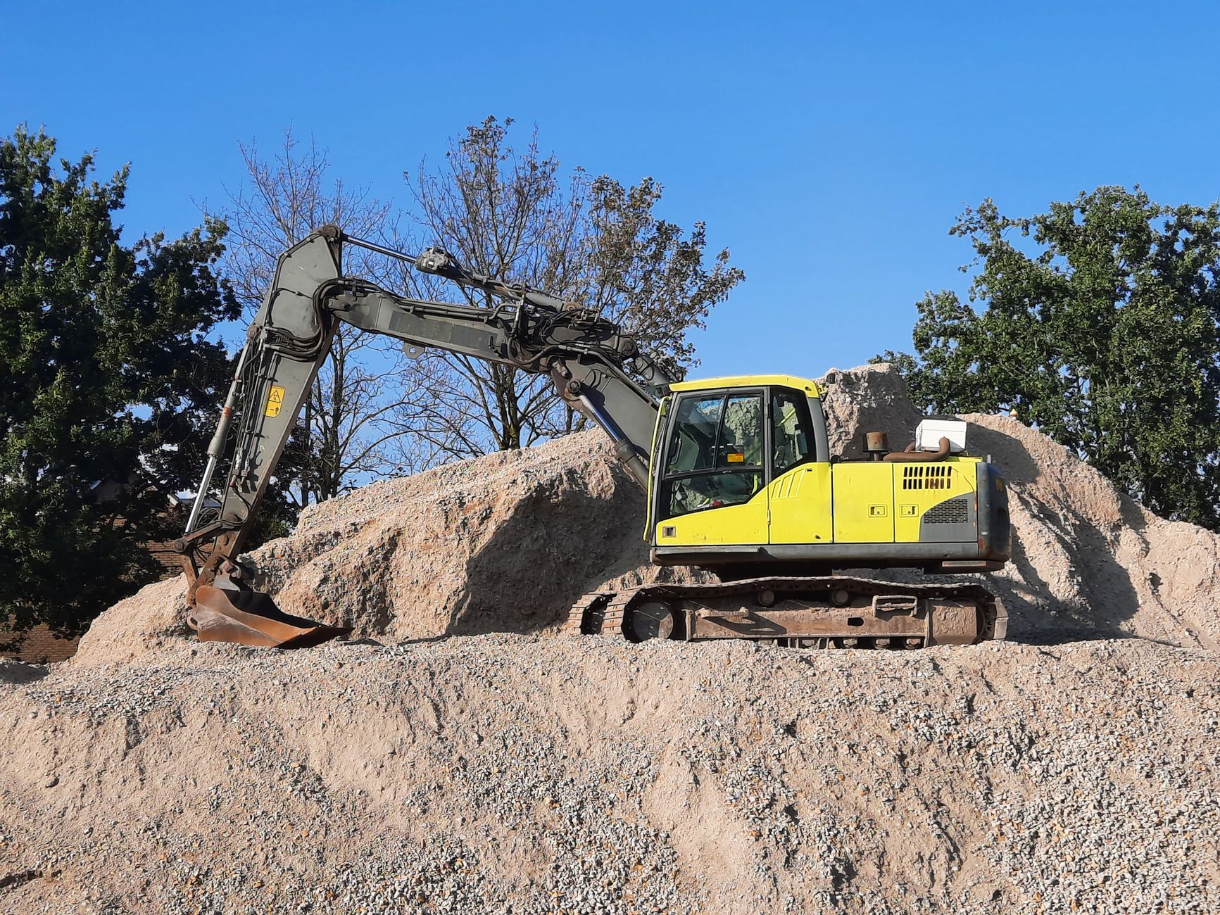 A yellow excavator working on a gravel mound at a construction site.