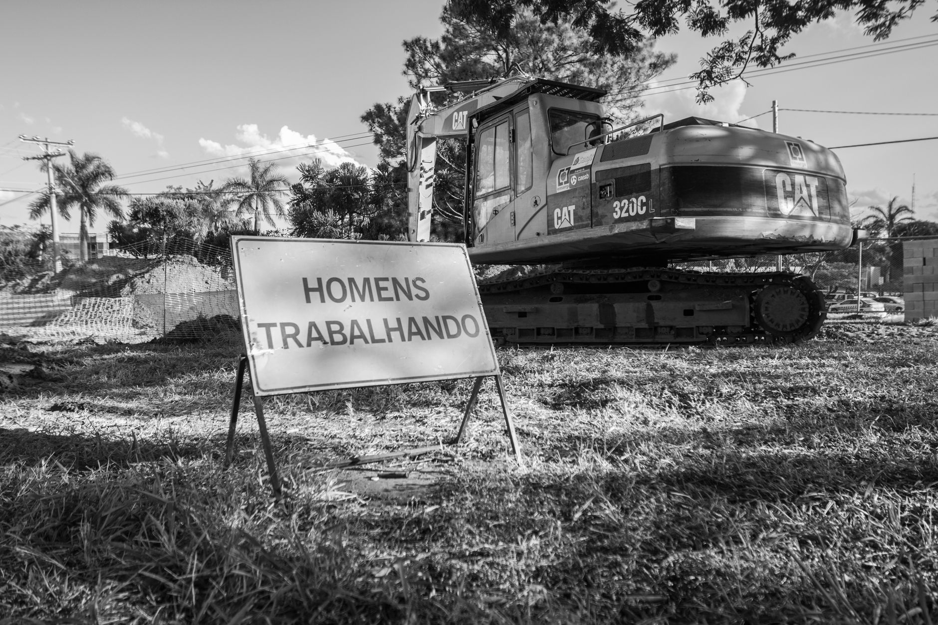 Black and white photo of a construction site featuring machinery and a sign in Portuguese.
