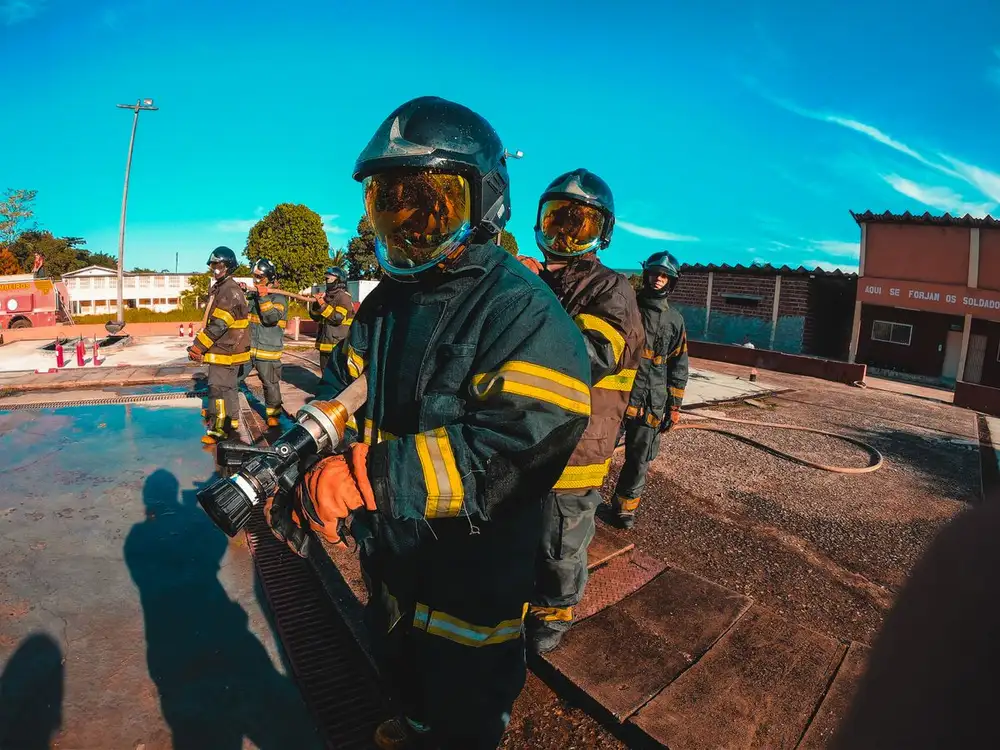 Firefighters in protective suits and helmets manage equipment during training outdoors.
